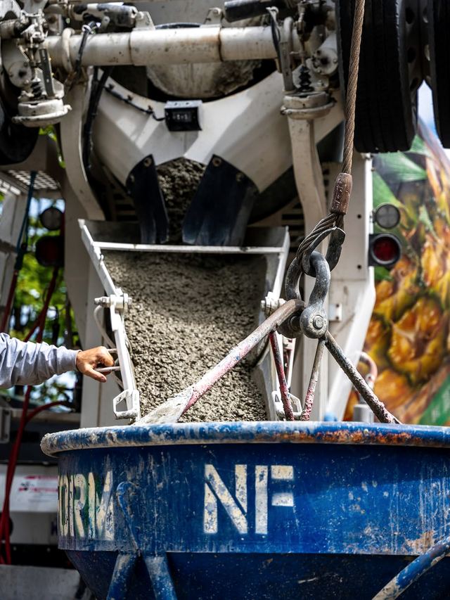 Fresh concrete pouring down a mixer chute into a blue Newform bucket
